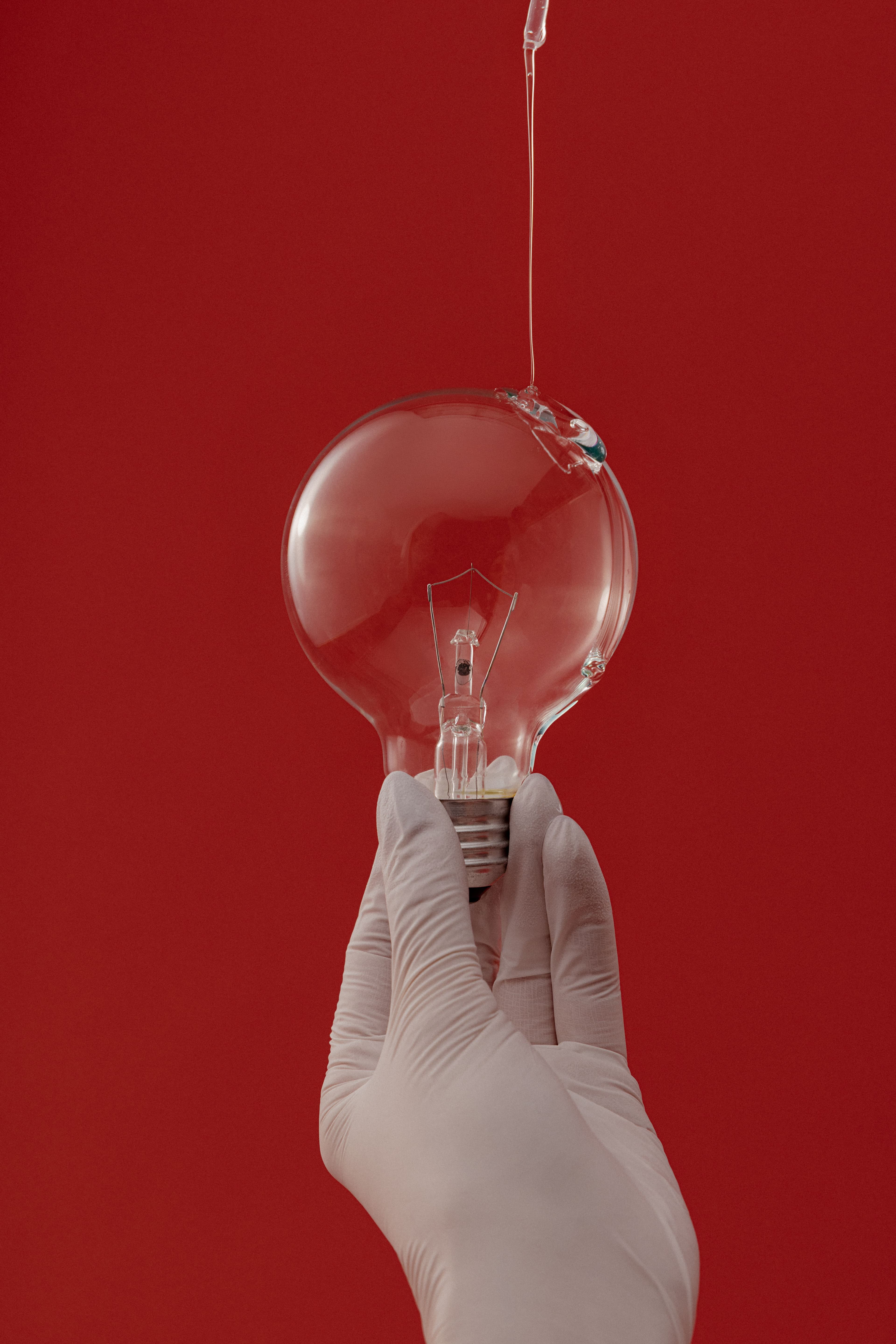 Light bulb with liquid dripping onto it against a red backdrop.
