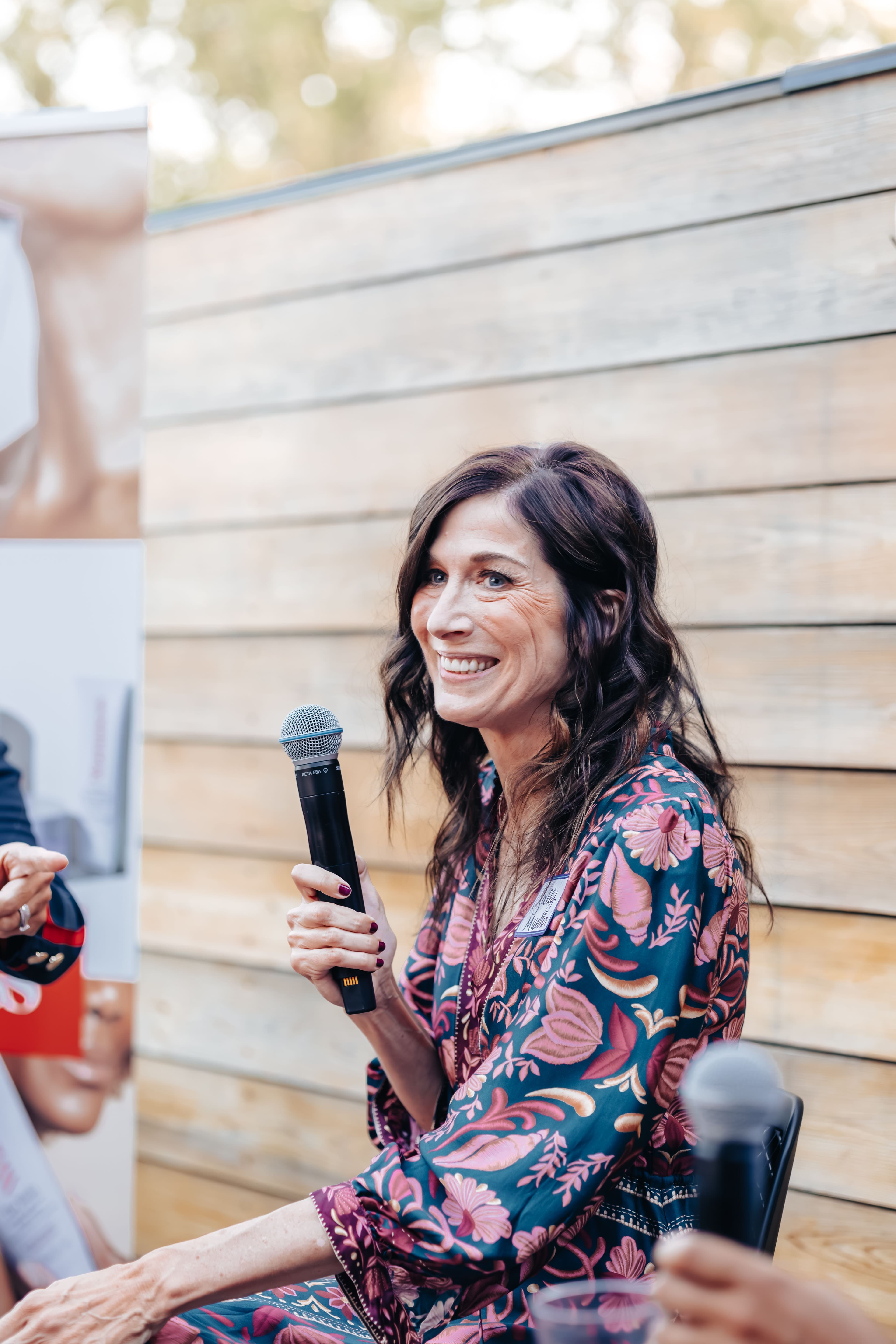 Woman holding a microphone smiling in a paisley dress.